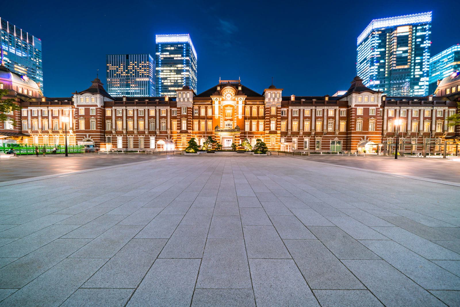 El edificio de ladrillo rojo de la estación de Tokio, lado Marunouchi, iluminado de noche entre torres de oficinas